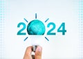 Green 2024 year numbers with creative trend light bulb assemble with earth holding by hand on white.