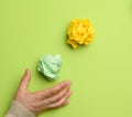 Green and yellow crumpled ball of paper and female hand on a green background Royalty Free Stock Photo