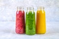 Green, yellow, purple smoothies in bottles of berries, greens, oranges on a white board on a gray table. Royalty Free Stock Photo