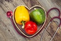 Green, yellow and red bell pepper with sthetoscope over rustic textured wooden background. Healthy vegetables, food.