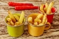 Green, yellow and red enameled cups with potato fries decorated with a red chilly pepper, over wooden table. Side view.