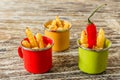 Green, yellow and red enameled cups with potato fries decorated with two cherry tomatoes, basil leaves, over wooden table.