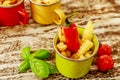 Green, yellow and red enameled cups with potato fries decorated with two cherry tomatoes, basil leaves and a red chilly pepper