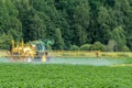 Green and yellow tractor fertilizing a green potato field