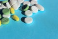 Green, yellow and white pills scattered on blue background. Helth and medical concept. Royalty Free Stock Photo