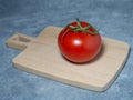 Greenhouse tomato on a small board. original size. Tomato in the kitchen. Ripe fresh vegetable on wooden kitchen utensils