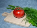 Greenhouse tomato on a small board. original size. Tomato in the kitchen. Ripe fresh vegetable on wooden kitchen utensils