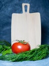 Greenhouse tomato on a small board. original size. Tomato in the kitchen. Ripe fresh vegetable on wooden kitchen utensils