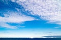 Greenlandic blue sky with altocumulus clouds over dark blue Arctic Ocean with iceberg, Greenland