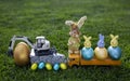 Composition of a model of an excavator, dump trucks, painted eggs, Easter bunnies standing on the grass