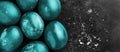 Greeting card with easter eggs painted in fluorescent glowing Aqua Menthe color on black background with white crumbs, egg shell