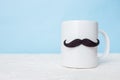 Greeting card fathers day holiday concept. White cup with mustache on blue pastel background