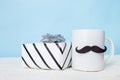 Greeting card fathers day holiday concept. White cup with mustache and gift box on blue pastel background Royalty Free Stock Photo