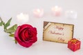 Greeting card with Happy Valentine`s Day text, single red rose, gift box, and candle light on white` Royalty Free Stock Photo