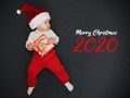 Little sleeping boy dressed as Santa Claus with a gift in his hands with the text Merry Christmas 2020 Royalty Free Stock Photo