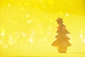 Greeting card in minimal style. Wooden Christmas tree on yellow background with copy space, lights bokeh, snow. New Year party. Royalty Free Stock Photo