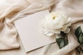 Greeting card mockup and beautiful beige peony flower on pastel beige fabric background with copy space.