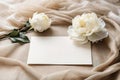 Greeting card mockup and beautiful beige peony flowers on pastel beige fabric background with copy space.