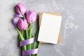 Greeting card mockup with envelope and tulip flowers bouquet with ribbon on grey concrete background