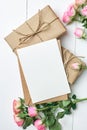 Greeting card mockup with fresh roses and gift boxes on white wooden background