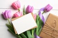 Greeting card mockup with gift box and tulip flowers bouquet with ribbon on white wooden background