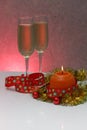 Greeting card template made of golden and green tinsel with red christmas balls, red ribbon, orange candle and two glasses of cham Royalty Free Stock Photo