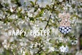 Greeting card with text Happy Easter in English. Decorative Easter bunny toy on background of blooming spring garden Royalty Free Stock Photo