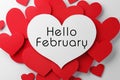 Greeting card with text Hello February. Many red paper hearts and one with text on white background, flat lay
