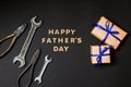 Greeting card to celebrate Father`s day. Two craft gifts with blue ribbons with tools on paper black background. Top view