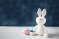 A greeting Easter card concept. Amigurumi handmade rabbit with Easter eggs on blue background. Copy space.