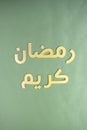 Greeting message: `May the month of Ramadan be blessed to you!` Golden arabic carved letters on a dark green background. Flat lay