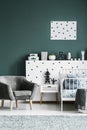 Grey armchair, bedside table, metal bed and dotted wall decorations in a dark green bedroom interior Royalty Free Stock Photo