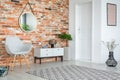 Grey armchair and cupboard in apartment interior with carpet and mirror on red brick wall Royalty Free Stock Photo