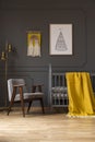 Grey armchair next to bed with yellow blanket in baby`s bedroom
