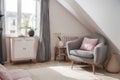 Grey armchair next to a wooden cupboard with dark vase in spacious, pink living room interior Royalty Free Stock Photo