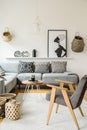 Grey armchair next to wooden table in bright interior with poster and cushions on sofa. Real photo Royalty Free Stock Photo