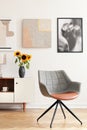 Grey armchair and sunflowers on cabinet in white living room interior with posters