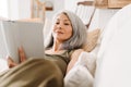 Grey asian woman reading book while lying on couch Royalty Free Stock Photo