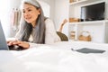 Grey asian woman smiling and using laptop on bed