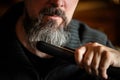 Grey bearded man with a straightener, beard styling and care at home