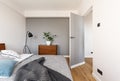 Grey blanket on bed in minimal bedroom interior with plant on wooden cabinet near door. Real photo