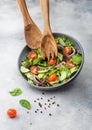 Grey bowl in motion with healthy fresh vegetables salad with lettuce and tomatoes, red onion and spinach on light background with Royalty Free Stock Photo