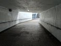 A grey, brutalist, concrete underpass leading down to a brightly lit entrance