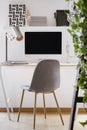 Grey chair at desk with desktop computer and lamp in modern white workspace interior. Real photo Royalty Free Stock Photo