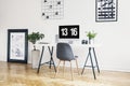 Grey chair at desk with desktop computer in white workspace interior with plants and posters. Real photo Royalty Free Stock Photo