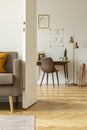 Grey chair at desk next to gold lamp in white home office interior with poster and sofa. Real photo Royalty Free Stock Photo