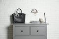 Grey chest of drawers with bag, books and decor elements near brick wall Royalty Free Stock Photo