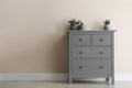 Grey chest of drawers with houseplants near wall. Space for text