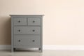 Grey chest of drawers near beige wall. Space for text