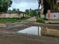 Grey color road constructed from cement surrounded with Indian styled homes in cloudy climate. Rain water covered the road after h